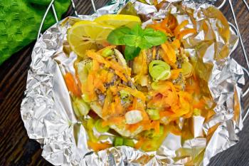 Pike with carrots, leek, basil and slices of lemon in foil on the lattice, a towel on the background of the wooden planks on top