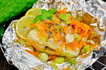Pike with carrots, leek, basil and slices of lemon in foil on the lattice, towel on a background of dark wood planks