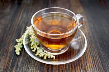 Herbal tea from wormwood in a glass cup on a saucer on a wooden boards background