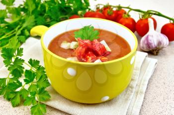 Gazpacho tomato soup in yellow bowl with parsley and vegetables on a napkin on the background of a granite table