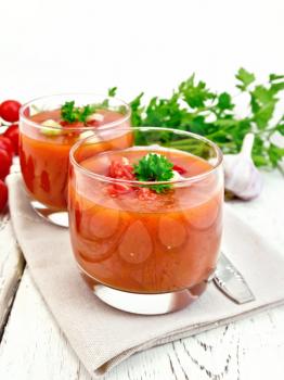 Gazpacho tomato soup in two glasses with parsley and vegetables on a towel on the background of wooden boards