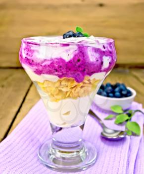 Milk dessert with blueberries, cornflakes, cottage cheese and a spoon on a towel on the background of a wooden board