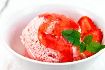 Ice cream strawberry in a white bowl with berries, mint and syrup against a light wooden board