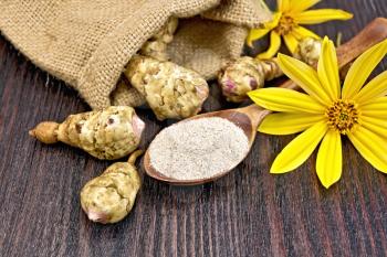 Flour of Jerusalem artichoke in a spoonful with flowers and vegetables in a bag on a wooden boards background