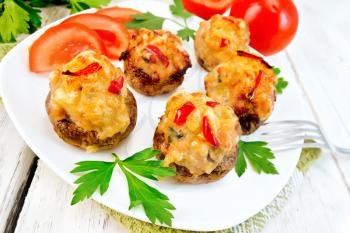 Mushrooms stuffed with meat and peppers with parsley and tomatoes in the white plate on a napkin, fork on the background of wooden boards