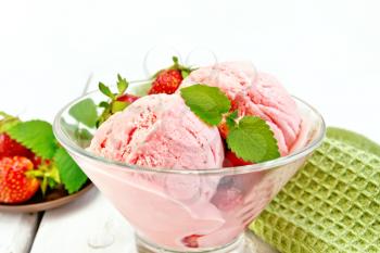 Strawberry ice cream in a glass bowl with berries and mint, green napkin on a light wooden board background