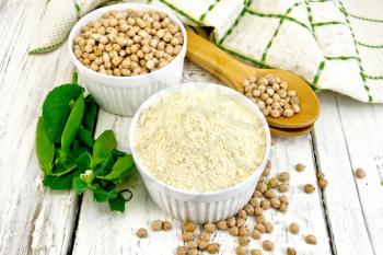 Flour chickpeas and chick-pea in white bowls and spoons, pods of green beans, a napkin on a wooden boards background