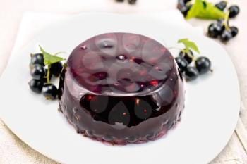 Jelly from a black currant with berries in a plate on a towel on the background of a stone table