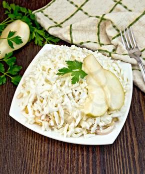 Salad of squid, rice, pears and eggs in a plate, parsley, napkin and fork on the background of wooden boards
