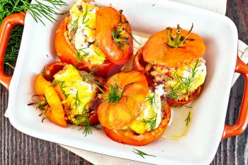 Tomatoes stuffed with meat and rice with cheese in a brazier on a napkin, parsley, dill and garlic on a wooden board background top