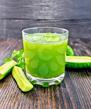 Cucumber juice in a glassful, vegetables and parsley on a wooden board background