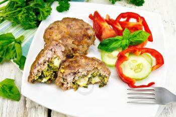 Cutlets stuffed with spinach and egg, salad with tomatoes, cucumber and pepper in a plate on a napkin, basil and parsley on a wooden board background