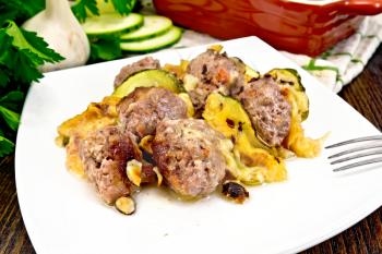 Meatballs baked with zucchini, cheese and nuts in a plate, napkin, garlic, parsley on a wooden board background