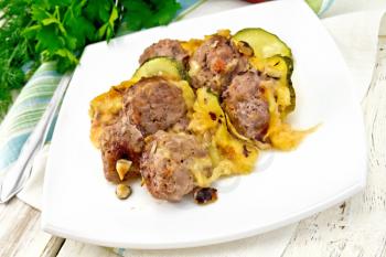 Meatballs baked with zucchini, cheese and nuts in a plate on a napkin, parsley on a light wooden board background