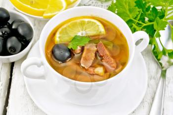 Soup saltwort with lemon, meat, pickles, tomato sauce and olives in a white bowl on a wooden board background