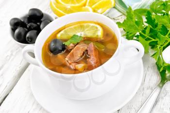 Soup saltwort with lemon, meat, pickles, tomato sauce and olives in a white bowl, parsley on a wooden board background