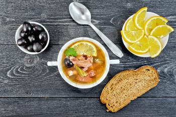 Soup saltwort with lemon, meat, pickles, tomato sauce olives in a bowl, bread and a spoon on the background of a wooden board from above