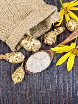 Flour of Jerusalem artichoke in a spoonful with flowers and vegetables in a bag on a background of wooden boards on top