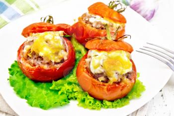 Tomatoes stuffed with meat and rice with cheese on lettuce in a plate, napkin, fork on a light wooden board background