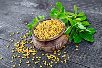 Fenugreek seeds in a bowl with green leaves on a wooden plank background
