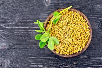 Fenugreek seeds in a clay bowl with green leaves on a wooden plank background
