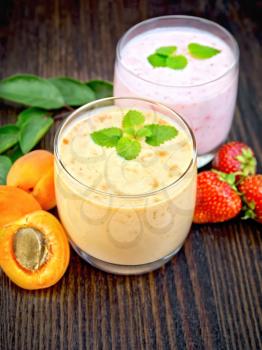 Two glasses of milkshake with apricots, strawberries and mint on the background of a dark wooden board