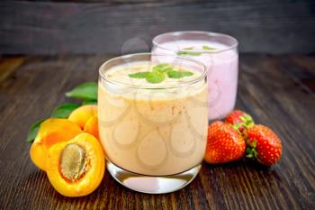 Two glasses of milkshake with apricots, strawberries and mint on a wooden plank background