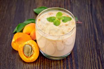 One glass of milkshake with apricots, mint on a wooden plank background