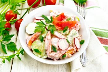 Salad of fresh tomatoes, cucumbers and radish with green onions and parsley,  flavored with mayonnaise and sour cream in a plate, towel and fork on the background of a light wooden board