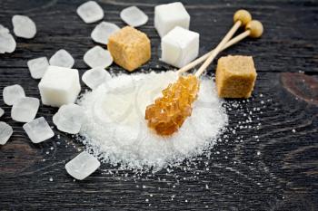 Sugar white and brown granulated, crystalline and cubes on the background of a black wooden board