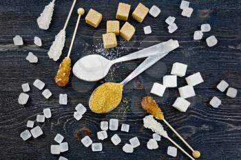 Sugar white and brown granulated in spoons, crystal and cubes on the background of a black wooden board from above