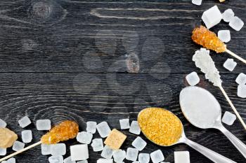 Sugar brown and white granules in a spoon, cubes and crystals on a stick in the form of a frame on the background of a black wooden board