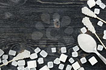 Sugar white granules in a spoon, cubes and crystals on a stick in the form of a frame on the background of a black wooden board