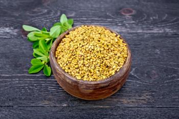 Fenugreek seeds in a clay bowl with green leaves on a background of a board