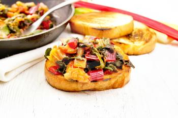 Toasted slice of bread with stewed leafy beet, onion and orange on a light wooden board background