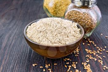 Flax flour in a bowl, white and brown linen seeds in two glass jars on a wooden board background
