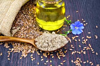 Flaxseed flour in a spoon, oil in a glass jar, blue linen flower and brown seeds in a bag on a wooden board background