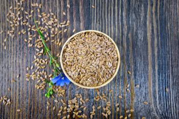 Seeds flaxen brown in a bowl, blue flax flower on a wooden board background from above