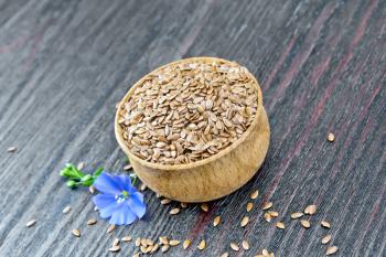 Seeds of linen brown in a bowl, a flax flower on a wooden plank background