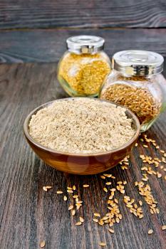 Flax flour in a bowl, white and brown linen seeds in two glass jars on the background of a dark wooden countertop