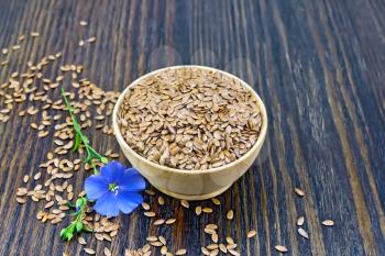 Seeds of linen brown in a bowl, a blue flax flower on a background of a dark wooden board
