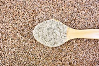 Flax flour in a wooden spoon on a background of brown flaxseed