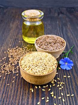 Linen seeds are white and brown in two bowls, linseed oil in a glass jar and blue flower on a wooden plank background