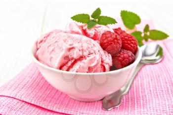 Ice cream crimson with raspberry berries and mint in white bowl, a spoon on pink towel on light wooden board background