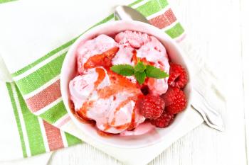 Ice cream crimson with raspberry berries, syrup and mint in white bowl, a spoon on napkin on wooden board background from above