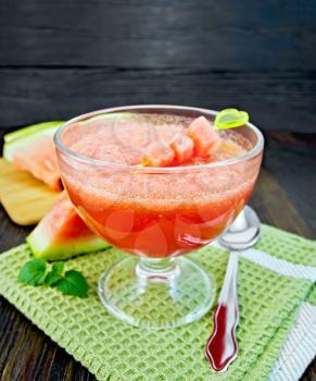 Jelly airy watermelon in a glass bowl, spoon and mint on a green towel on a wooden plank background