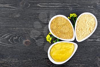 Mustard sauce, seeds and mustard powder in three saucepans, flowers on the background of a wooden board from above