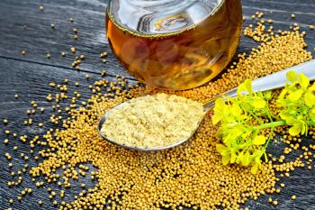 Mustard powder in a metal spoon, oil in a glass jar, seeds and mustard flower on a wooden board background