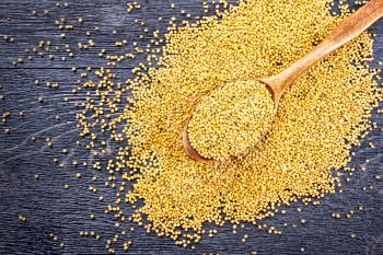 Mustard seeds in a spoon and on a table on the background of a black wooden board from above