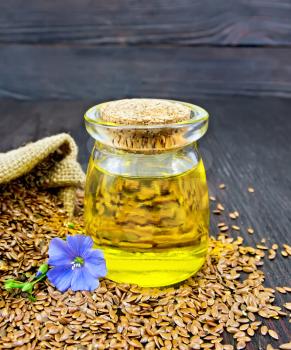 Linen oil in a glass jar with seeds in a bag and on a table, blue flax flower on a background of a dark wooden board